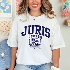 Celebrate your law school victory with our Juris Doctor Custom Graduation Year Comfort Colors® Lawyer Shirt! Aspiring legal eagles and accomplished advocates, rejoice! Mark your momentous law school achievement with this ultra-comfy lawyer tee, featuring bold Juris Doctor varsity letters and a graduation crest showcasing iconic legal symbols. Crafted from premium, garment-dyed Comfort Colors® fabric, it's the perfect way to celebrate your graduation in unparalleled style and comfort. Why this Juris Doctor t-shirt stands out: - Eye-catching Juris Doctor varsity lettering: Declare your hard-earned title in a classic collegiate font, instantly recognizable and attention-grabbing. - Symbolic crest: Packed with powerful legal icons - the Scales of Justice representing fairness, a stack of Books Collegiate Tops With University Logo For Campus, Varsity Tops With University Logo For Campus, Campus Fan Apparel T-shirt With Letter Print, White Text Print T-shirt For Campus, Casual University Logo Tops For School, Casual Tops With University Logo For School, School Spirit Tops With Letter Print For Campus, School Spirit Letter Print Tops For Campus, Campus Letter Print Tops For School Spirit