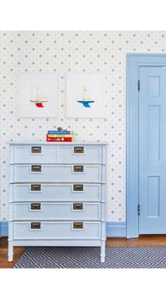 a blue dresser sitting in front of a wallpapered wall with boats on it