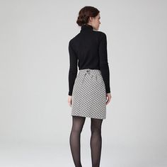 a woman is standing in front of a white background wearing a black sweater and patterned skirt