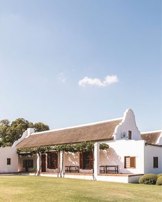 a white house with a thatched roof and picnic tables in the front yard area