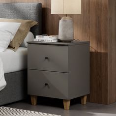 a night stand with two drawers and a lamp next to it on top of a bed