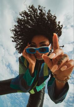 a woman wearing sunglasses and pointing to the sky