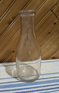 an empty glass bottle sitting on top of a blue and white table cloth next to a wooden wall