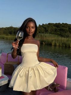 a woman in a white dress holding a glass of wine while sitting on a boat