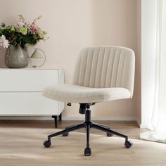 a white office chair sitting in front of a vase with flowers on top of it