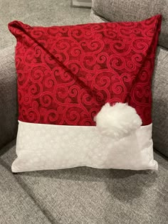 a red and white pillow sitting on top of a gray couch with a pom - pom