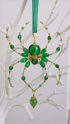 a green spider ornament hanging from a tree branch with beads and chains attached to it