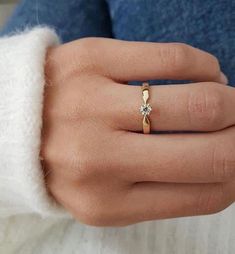 a woman's hand wearing a gold ring with a diamond on the middle finger