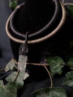 a necklace with a crystal point hanging from it's center surrounded by green leaves