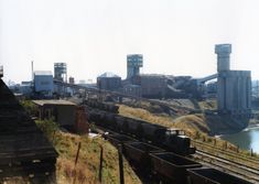 there is a train that is going down the tracks by some water and buildings in the background