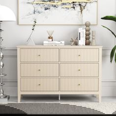 a white dresser sitting next to a large painting on the wall in a living room