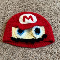 a crocheted red hat with eyes on the top is laying on the carpet