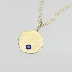 Handcrafted 14k yellow gold necklace with a pendant made of recycled gold. The scrap metal was melted into a chunk, hammered flat, stamped, polished, drilled, and given a hammered texture. A 2mm AA grade round faceted sapphire stone is flush set into the pendant. Comes on your choice of a 16 or 18 inch 14k yellow gold chain with the artist's tag attached at the clasp. (Shown on 16 inch chain on model) Can also be purchased as the pendant alone. Sapphire is the birthstone for September. Pendant m Gold Sapphire Round Pendant Necklace, Yellow Gold Sapphire Round Pendant Necklace, Gold Sapphire Round Birthstone Necklace, Yellow Gold Sapphire Round Birthstone Necklace, Yellow Gold Sapphire Birthstone Necklace, Gold Sapphire Birthstone Necklace, Hammered Yellow Gold Necklace In Recycled Material, Hammered Yellow Gold Necklace In Recycled Gold, Yellow Gold Hammered Necklace In Recycled Gold