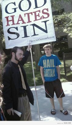 a man holding a sign that says god hates sin while standing next to other people