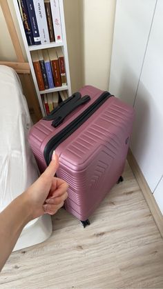 a person is reaching for a piece of luggage on the floor in front of a bookcase