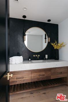 a bathroom with black and white walls, wooden cabinets and a round mirror