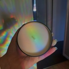 a person holding a cup with a rainbow light on the wall in the back ground