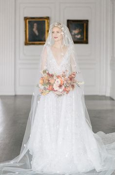 a woman in a white wedding dress holding a bouquet and wearing a bridal veil