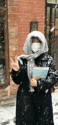 a woman wearing a face mask while standing in the snow with her hands out and holding a book