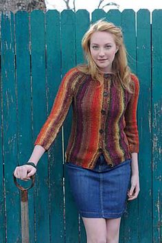 a woman standing in front of a green fence holding an old fashioned walking stick and smiling at the camera