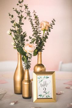 two vases with flowers and greenery are sitting on a table