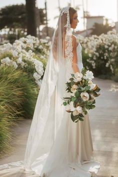 a woman in a wedding dress and veil holding a bouquet with white flowers on it