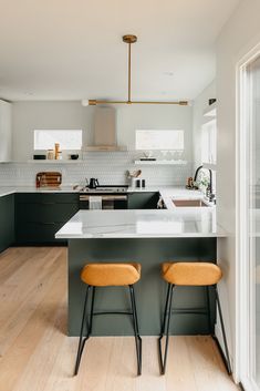 two stools are in front of the kitchen island and countertop, which is painted dark green