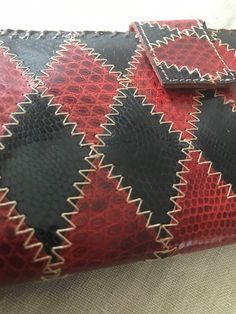 a red, black and white clutch bag on a bed with a pillow behind it