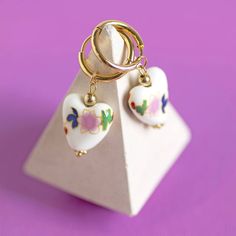 A beautiful pair of white porcelain heart huggie earrings with floral detail. These lovely earrings feature porcelian style ceramic glazed heart with a subtle floral design suspended from gold plated huggie hoops. The earrings would make a lovely gift, treat for yourself and certainly a welcome addition to any jewellery collection. Presented in a an organza gift bag with the sentiment card of your choice. If you would like to upgrade your purchase to include a gift box please order here: https:/ Porcelain Heart, Heart Hoop Earrings, Wedding Keepsakes, Huggie Earrings, Blue Pearl, Pearl Flower, Organza Gift Bags, Lovely Earrings, Jewellery Collection