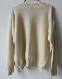 a white sweater hanging on a hanger with a red hook attached to it's side