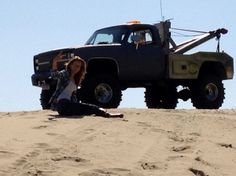 a woman sitting on top of a sandy hill next to a black truck with a crane in the back