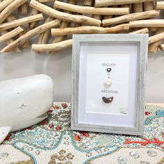 a white frame holding two different types of earrings on a table next to driftwood