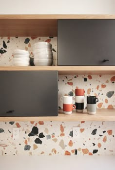 two shelves with cups and plates on them in front of a wallpapered background