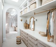 a white closet with lots of clothes and baskets on the shelves