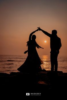 two people are dancing on the beach at sunset