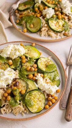 two plates with pasta, cucumbers and chickpeas on them next to silverware