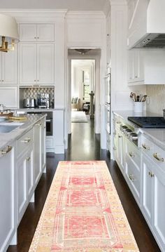 a kitchen with white cabinets and an orange runner rug in the middle of the room