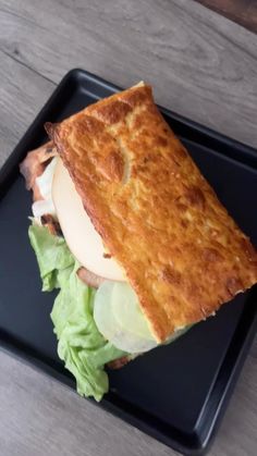 a sandwich with lettuce and an egg on a black plate sitting on a wooden table