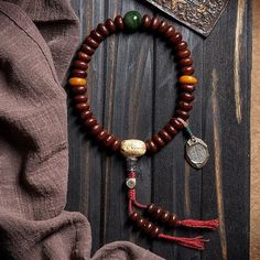 a wooden beaded bracelet with two charms and a medallion on it next to a scarf