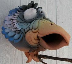 a ceramic bird with its mouth open on a white wooden wall behind it is a branch