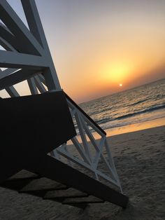 the sun is setting over the ocean and beach chairs are on the sand near the water