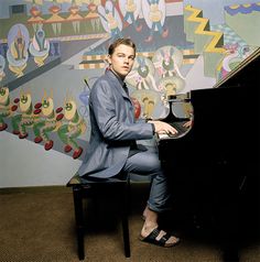 a man sitting at a piano in front of a wall with colorful paintings on it