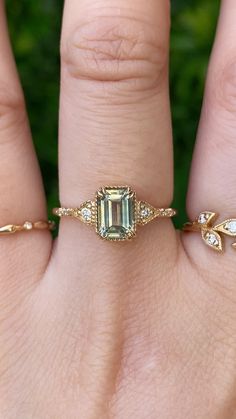 a woman's hand with two rings on it and an emerald stone in the middle