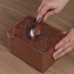 a person scooping chocolate from a container with a spoon in it on a wooden table