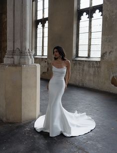 a woman in a white wedding dress standing next to a tall columned building with large windows