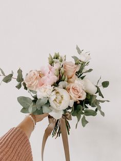 a woman holding a bouquet of flowers in her hand with white and pink roses on it