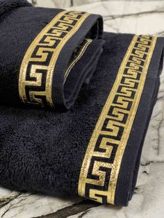 two black towels with gold greek designs on them sitting on a marble counter top next to each other