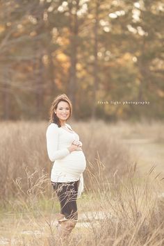 a pregnant woman standing in tall grass with her hands on her belly