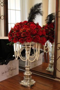 red roses and pearls in a silver candelabra on a wooden table next to a mirror