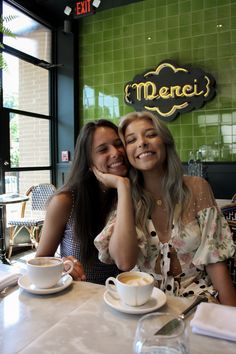 two women sitting at a table with cups of coffee in front of them, smiling